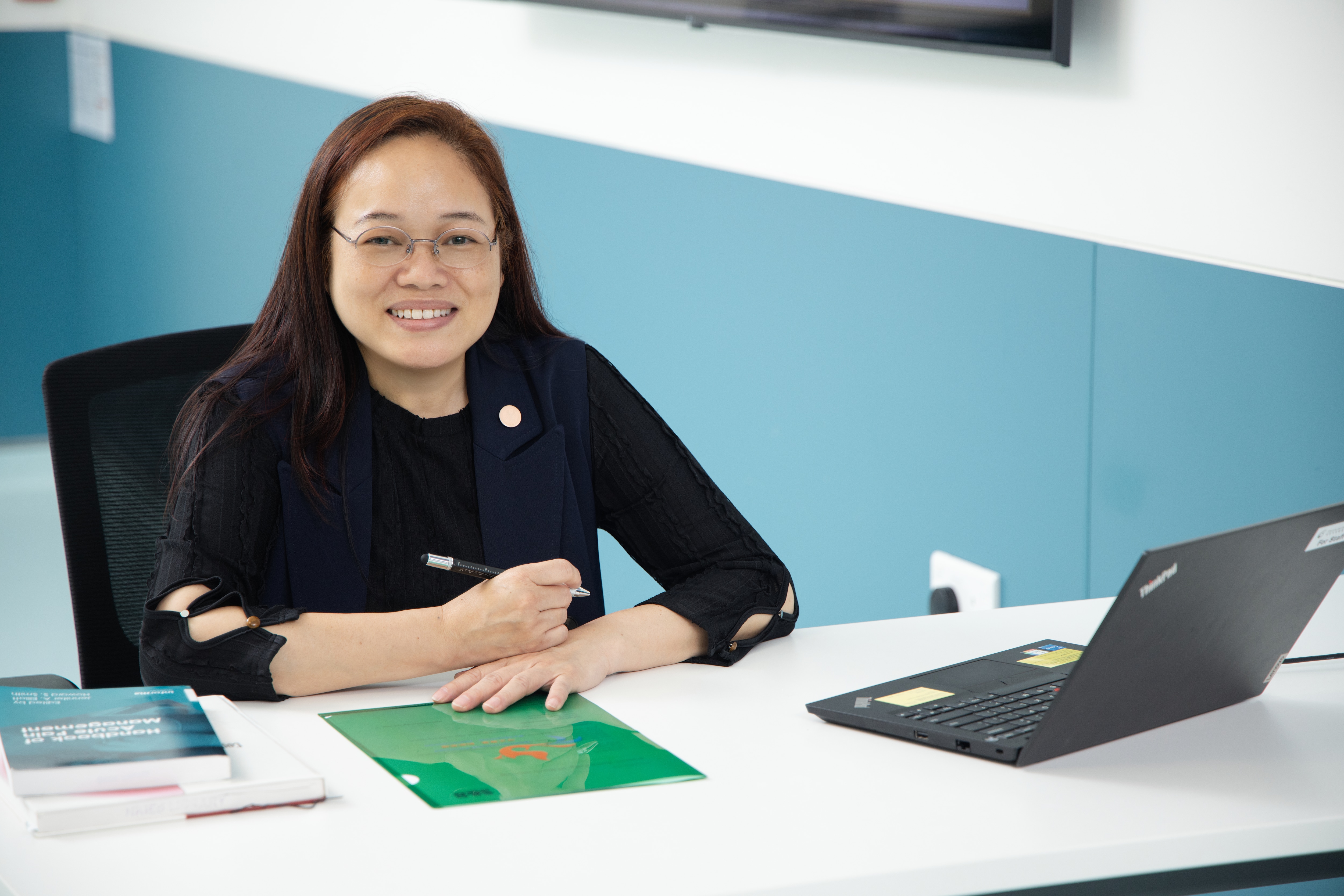 Woman (Sunne Fong) on desk with pen and laptop